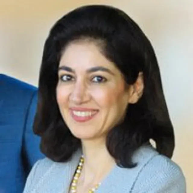 The image shows a woman dressed in business attire with a confident expression, standing beside a man who appears to be in a formal setting.