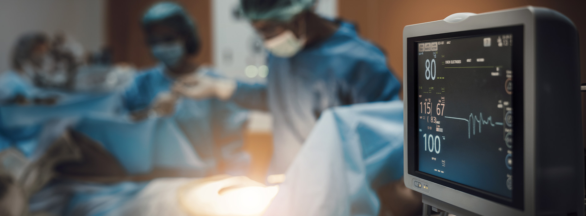 The image depicts a medical setting with healthcare professionals engaged in patient care, focusing on a digital monitor displaying various medical readings.