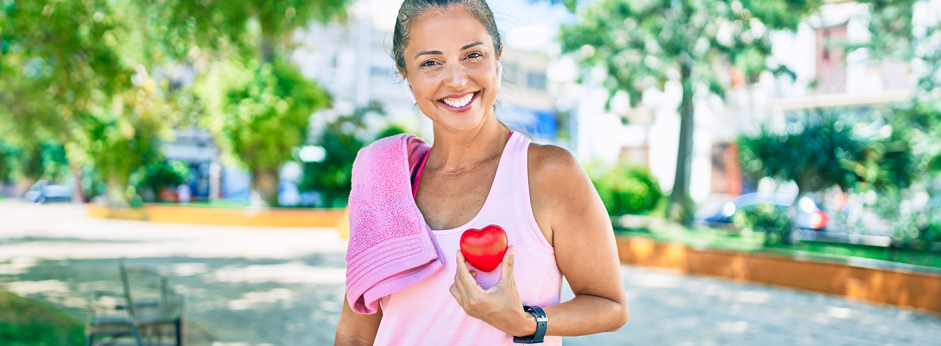 The image features a woman standing outdoors with a towel draped over her shoulder and a sports ball in her hand, smiling at the camera.