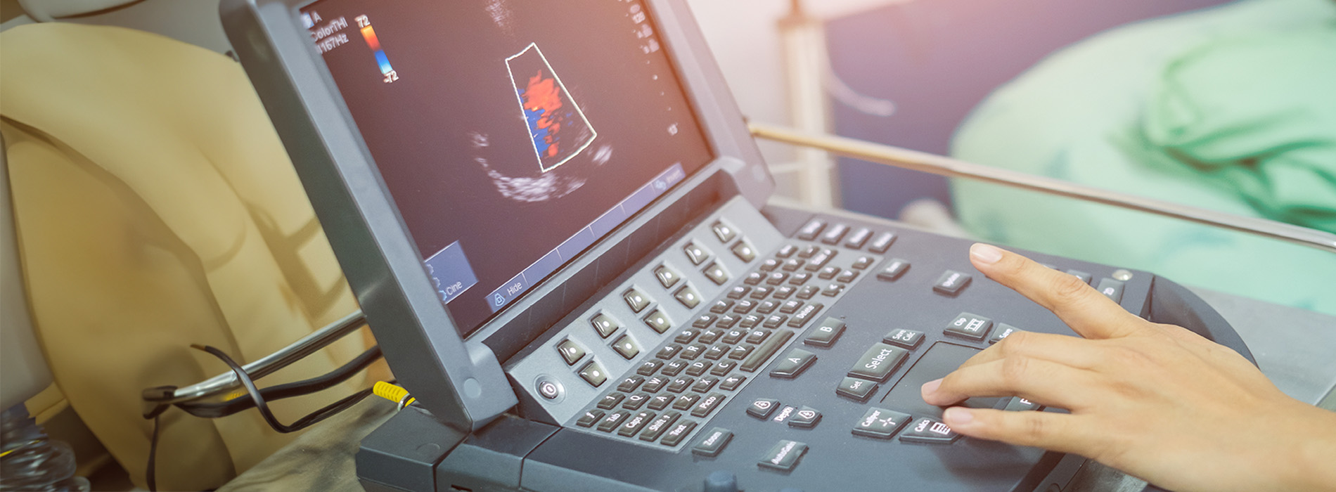 The image depicts a medical setting with a person operating an ultrasound machine while viewing its screen.