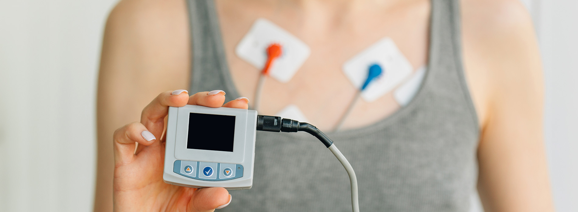 An adult holding a medical device with electrodes attached to their chest, showcasing a heart rate monitor.