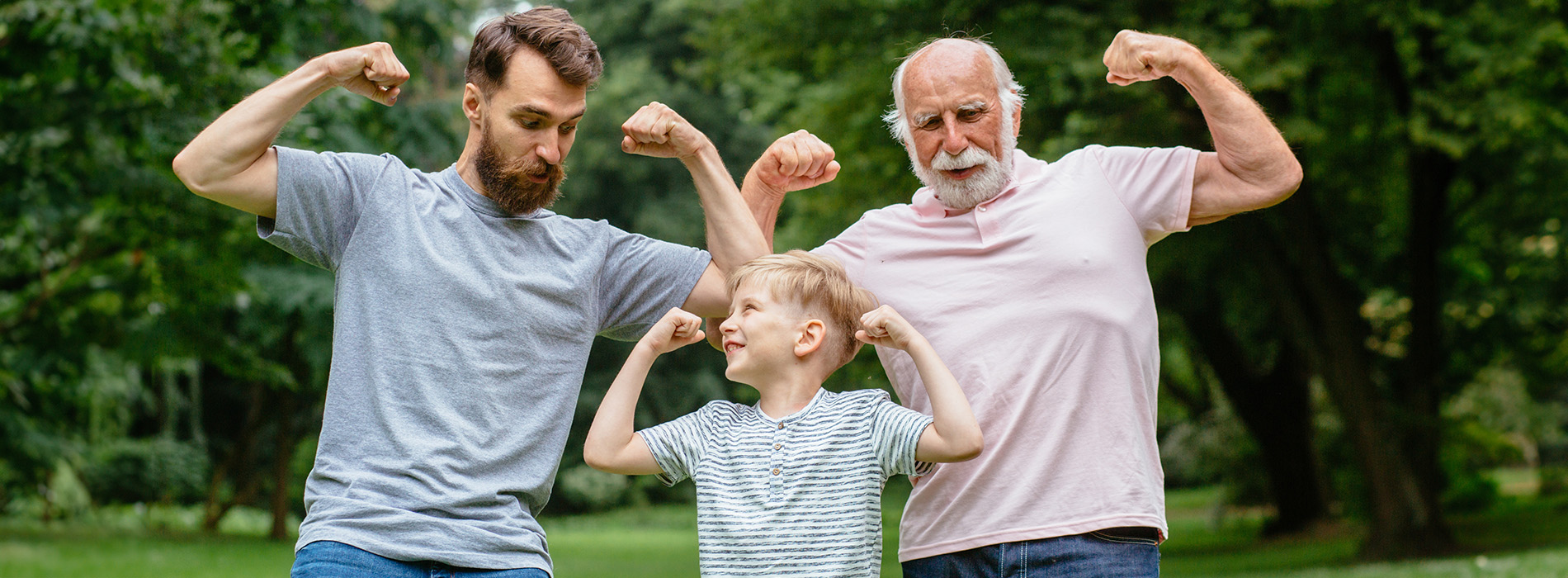 The image shows three people posing together outdoors two adults are flexing their muscles while standing with a child, who appears to be watching them.