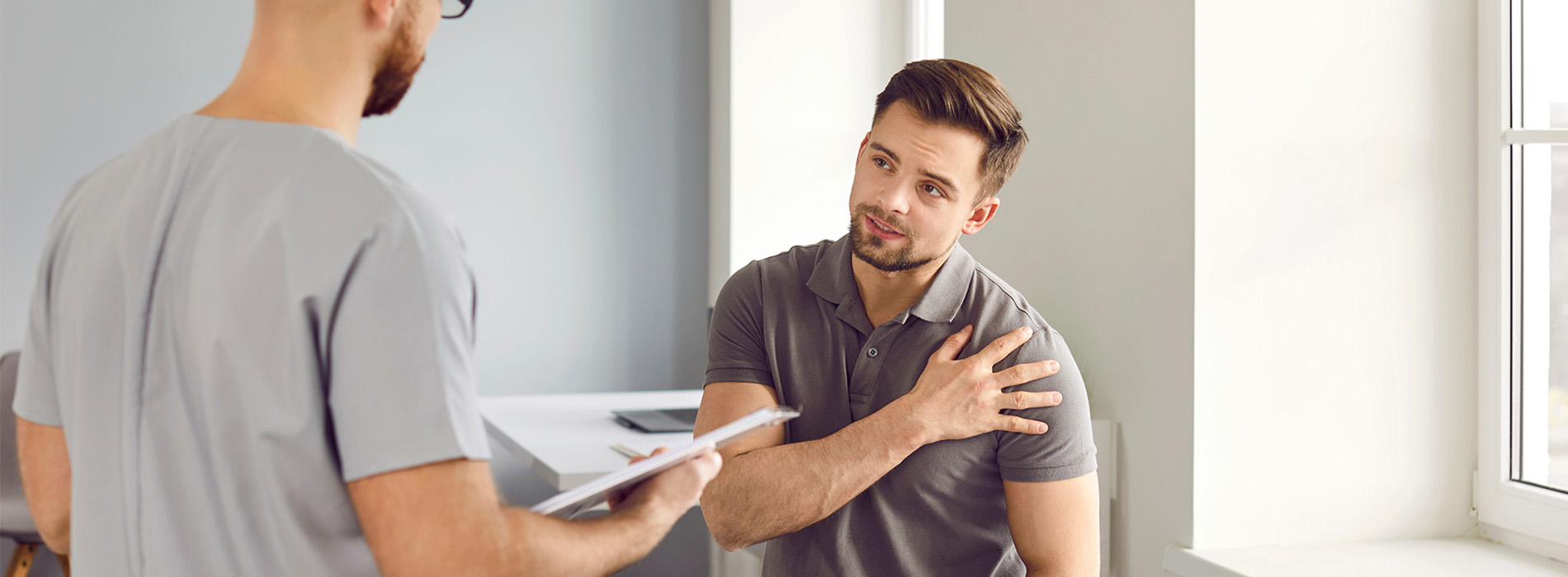 A man in a suit talking with a seated male nurse.