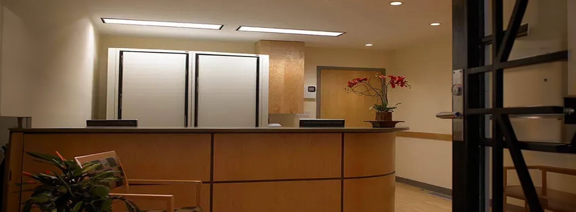 The image shows a modern office reception area with a counter, a backdrop of a wall with framed pictures, and a view into an open workspace beyond the reception desk.
