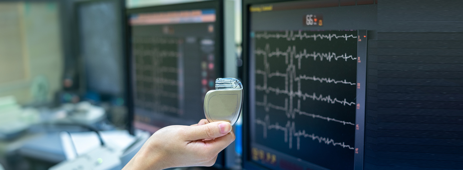 A person holding a small device near a large computer screen displaying medical data.