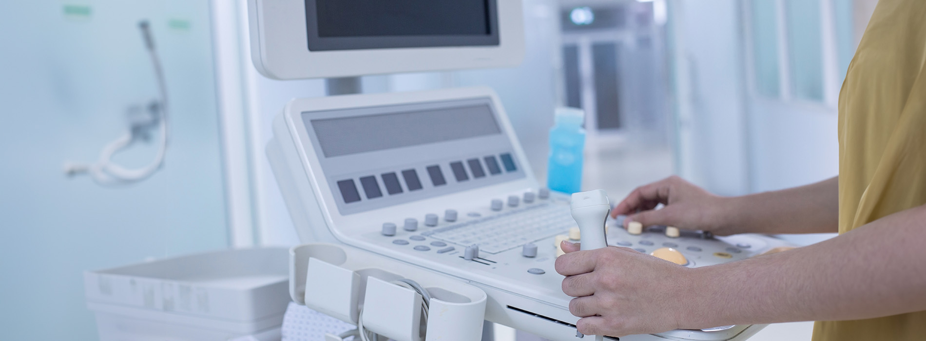 The image shows a person standing at an electronic medical device with various buttons and screens, possibly a nurse or healthcare professional attending to their duties.