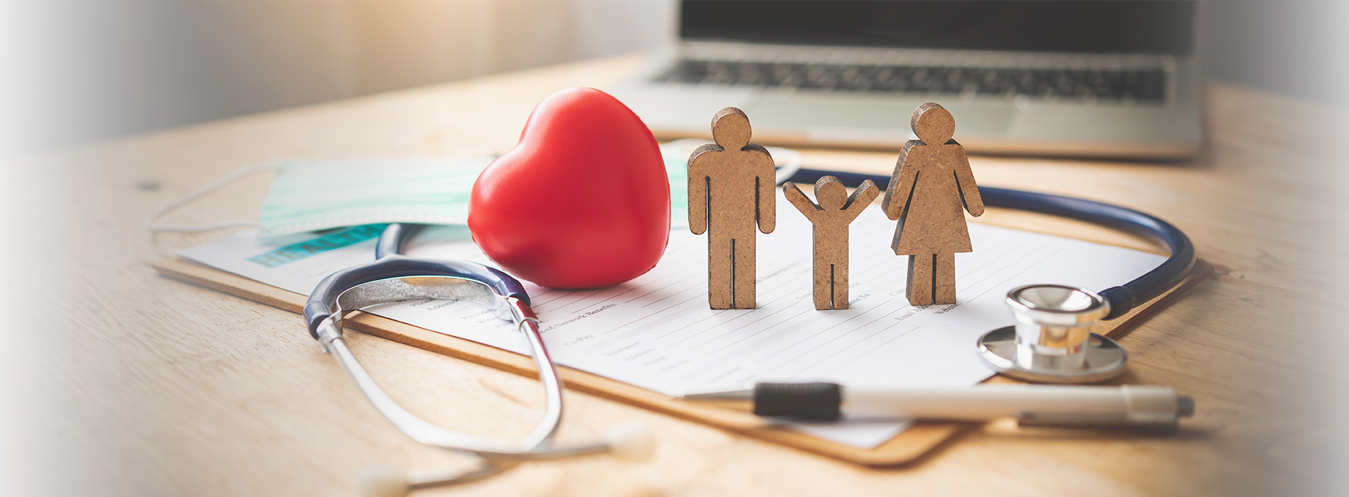 The image shows a collage with a heart-shaped object, medical equipment, and figures representing people, all placed on a surface with a laptop and other items.