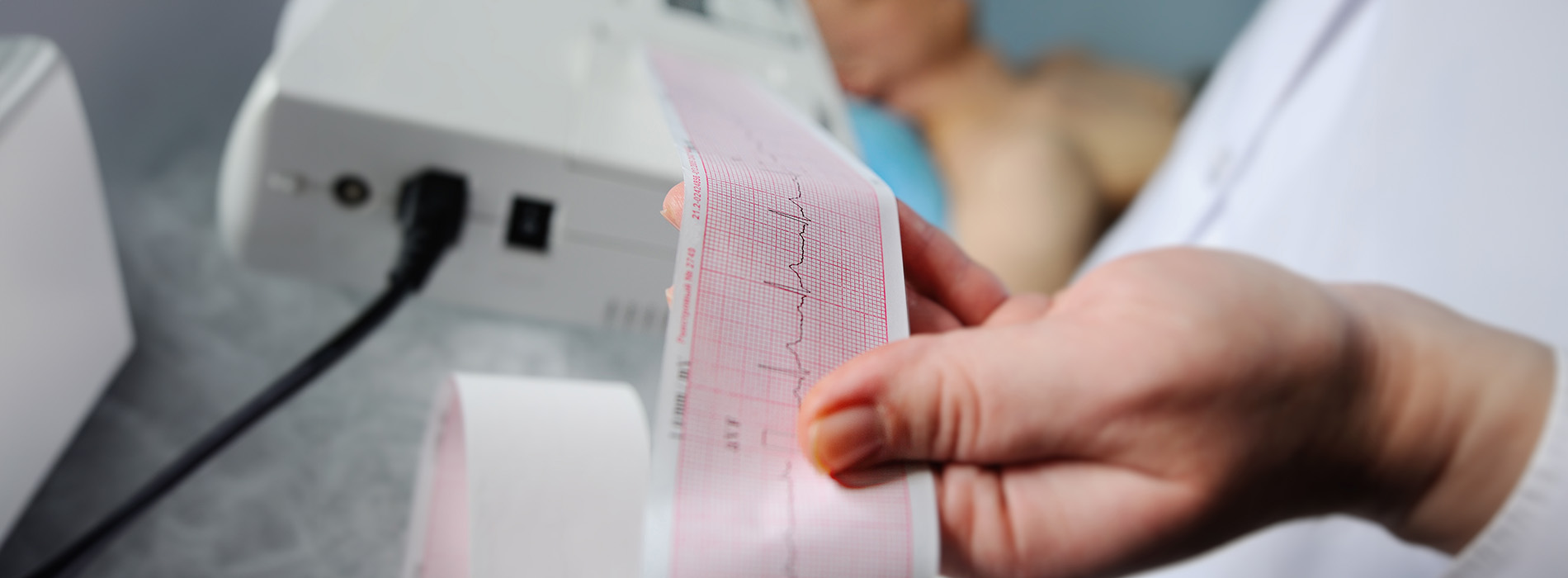 A person s hand holding a strip of paper with printed data, being read by a machine in a laboratory setting.