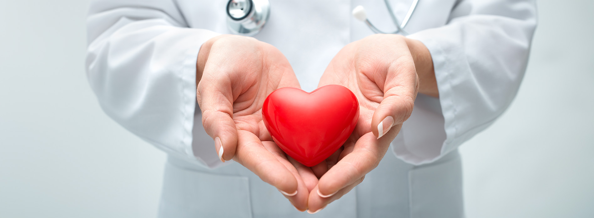 The image shows a person wearing a white lab coat holding a red heart with both hands, conveying a message related to healthcare or love.